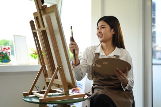 Attractive female artist painting with watercolor on canvas in art workshop. Art, creative hobby and leisure activity concept.