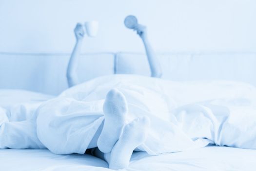 Female hand holding cup of coffee from under a blanket in bed. Woman waking up in the morning.