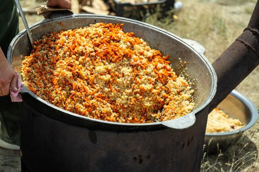 Cooking traditional oriental pilaf in large cauldron on a sunny day outdoor. Real kazakh pilaf in the steppe.