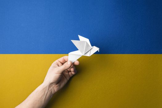 hand holding white paper bird against background of yellow blue flag of ukraine. concept needs help and support, truth will win