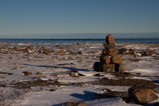 Arctic landscape - an Inuksuk or Inukshuk landmark on a snow covered arctic tundra in Nunavut on a clear sunny day, near Arviat, Nunavut, Canada