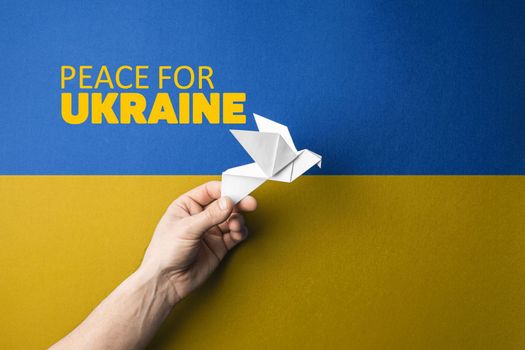 hand holding white paper with words peace for Ukraine on blue and yellow background