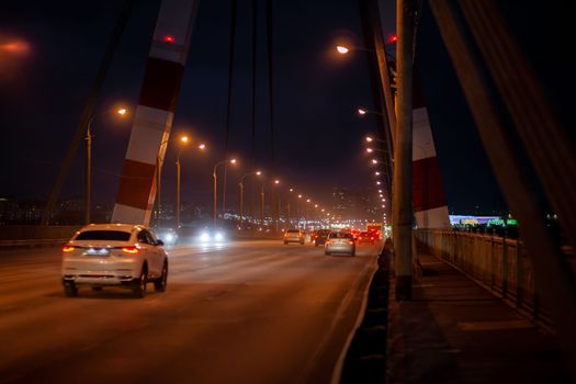 29.11.2022, Cherepovets, Russia. A large automobile bridge on which cars drive at night. A bridge with large columns and lighting. Cars are driving over the bridge