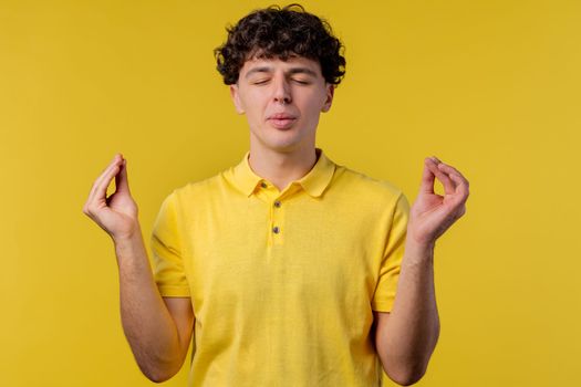 Calm man relaxing, meditating, refuses stress. Curly haired guy breathes deeply, calms down yellow studio background. Yoga, moral balance, zen concept. High quality photo