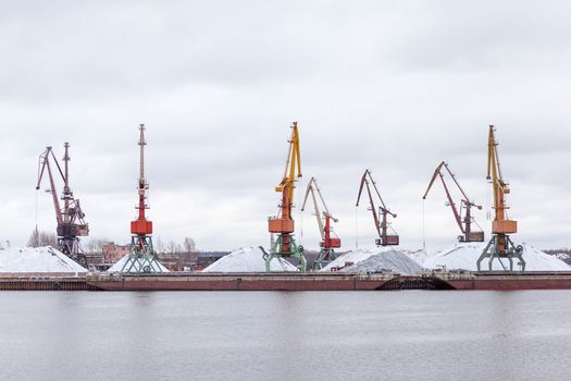 River port in winter. Port cranes on the bank of the river. Embankment of the river port, a barge at the quay wall. Large port cranes on the river. Extraction and transportation of sand other cargo