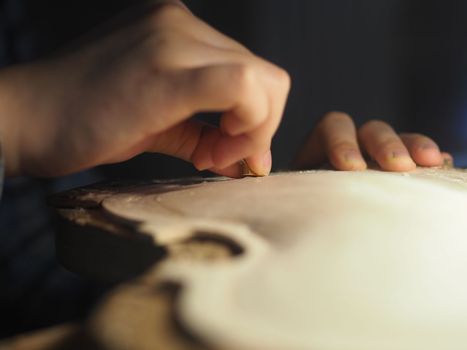 artisan working on raw wood violin plate with finger plane on the bench