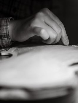 artisan working on raw wood violin plate with finger plane on the bench
