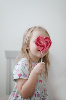 Beautiful little girl holding a big heart shaped lollipop.