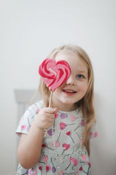 Beautiful little girl holding a big heart shaped lollipop.