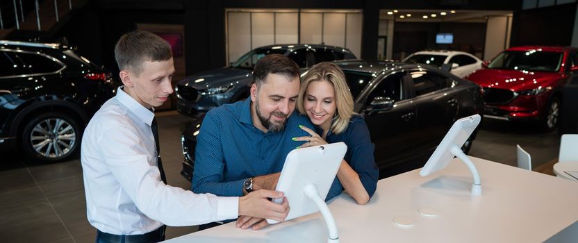 Caucasian married couple chooses a car in a car dealership on digital tablets