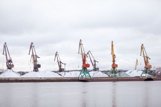 River port in winter. Port cranes on the bank of the river. Embankment of the river port, a barge at the quay wall. Large port cranes on the river. Extraction and transportation of sand other cargo