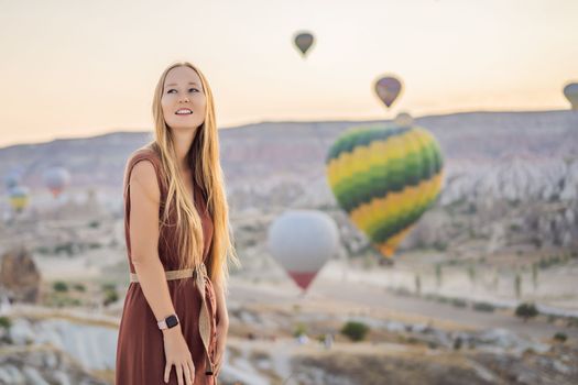 Tourist woman looking at hot air balloons in Cappadocia, Turkey. Happy Travel in Turkey concept. Woman on a mountain top enjoying wonderful view.