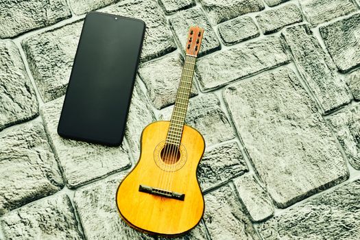 an application, especially as downloaded by a user to a mobile device. Mobile phone and acoustic guitar on a gray silver brick surface. High quality photo