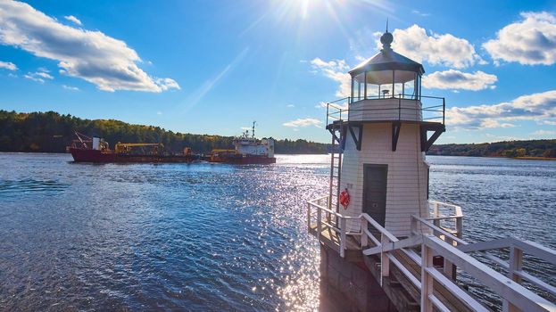Image of Large commercial ship on Maine river sails past small lighthouse with blue skies