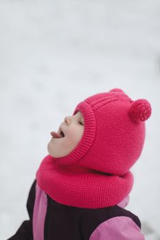 Funny little girl eating snow on winter day. Kids cold and flu concept. Tongue in snow