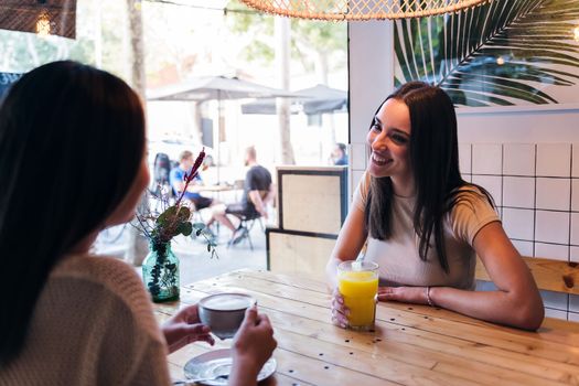 smiling young caucasian woman drinking a juice with a friend in a coffee shop, concept of friendship and love between women