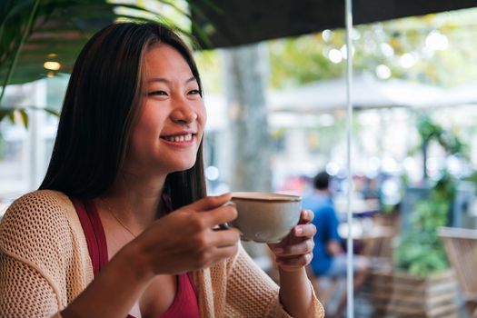 smiling young asian woman drinking coffee in a coffee shop, concept of relaxation and leisure