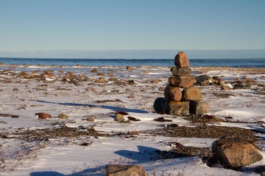 Arctic landscape - an Inuksuk or Inukshuk landmark on a snow covered arctic tundra in Nunavut on a clear sunny day, near Arviat, Nunavut, Canada