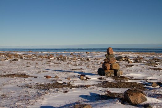 Arctic landscape - an Inuksuk or Inukshuk landmark on a snow covered arctic tundra in Nunavut on a clear sunny day, near Arviat, Nunavut, Canada