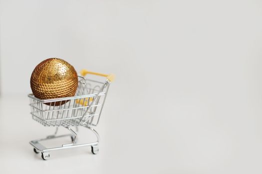 Small shopping cart with christmas ball on white background. Creative idea for shopping online, winter sale, supermarket, discount promotion and Black Friday concept. New Year and Christmas shopping