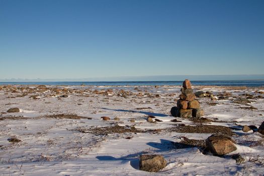 Arctic landscape - an Inuksuk or Inukshuk landmark on a snow covered arctic tundra in Nunavut on a clear sunny day, near Arviat, Nunavut, Canada