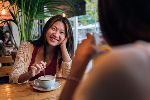 young asian woman smiling in love to her friend during their date in a coffee shop, concept of friendship and love between women