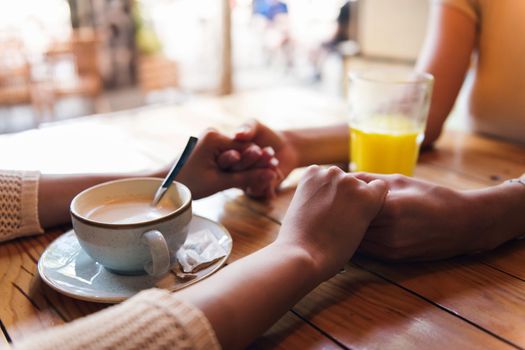 close-up of two women in love holding hands during their date in a coffee shop, concept of friendship and love between women