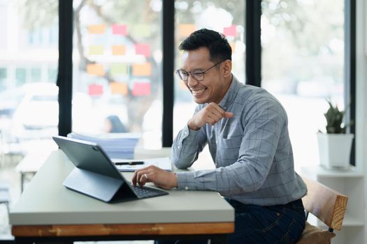 Portrait of a man business owner showing a happy smiling face as he has successfully invested her business using computers and financial budget documents at work.