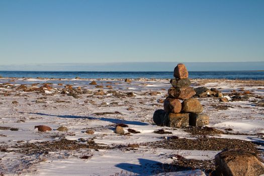 Arctic landscape - an Inuksuk or Inukshuk landmark on a snow covered arctic tundra in Nunavut on a clear sunny day, near Arviat, Nunavut, Canada