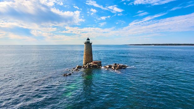 Image of Lone stone lighthouse tower in middle of water with collapse rock rubble in Maine