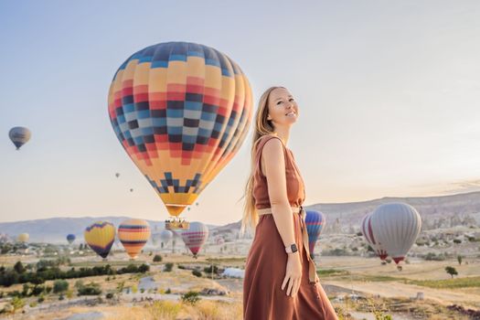 Tourist woman looking at hot air balloons in Cappadocia, Turkey. Happy Travel in Turkey concept. Woman on a mountain top enjoying wonderful view.