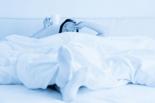 Female hand holding cup of coffee from under a blanket in bed. Woman waking up in the morning.