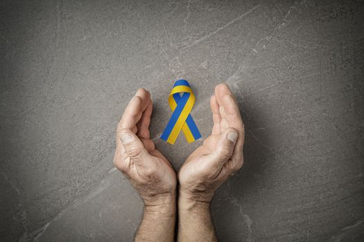 male hands with yellow and blue ribbon on marble background. concept needs help and support, truth will win