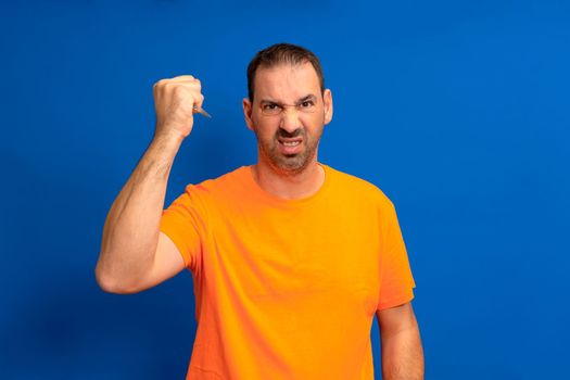 Hispanic man with beard holding scissors over isolated blue background annoyed and frustrated screaming with anger, crazy and yelling with raised hand, anger concept