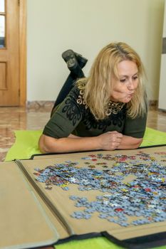 Caucasian blonde woman lying on the floor grimacing with her mouth in worry that she won't be able to complete the puzzle she is doing