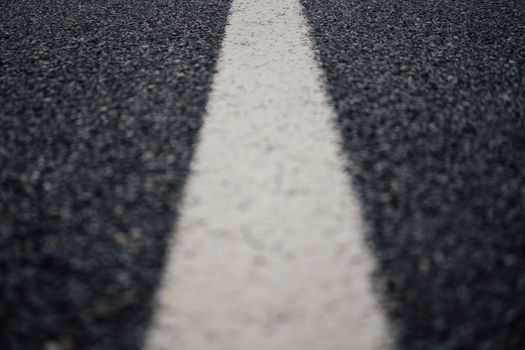 Low angle close-up of a white paint line on the center of a black asphalt road.