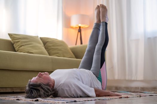 senior woman doing warmup workout at home. Fitness woman doing stretch exercise stretching her body. Elderly woman living an active lifestyle. 