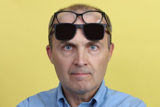 Satisfied attractive man 40-55 years old in a blue shirt on a yellow background with two glasses on his face.