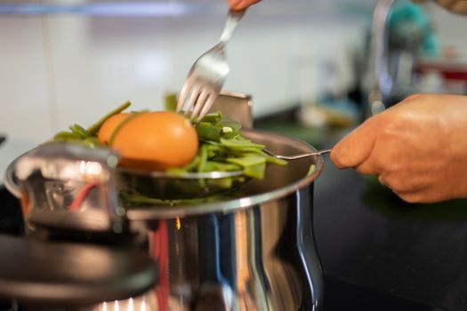 woman hands taking boiled eggs and green beens out of cooking pot with a fork and spoon.