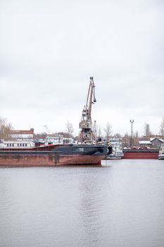 River port in winter. Port cranes on the bank of the river. Embankment of the river port, a barge at the quay wall. Large port cranes on the river. Extraction and transportation of sand other cargo