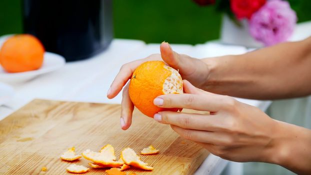 summer, in the garden, close-up, female hands are peeling an orange from the peel. family holidays, lunch on the nature, in the courtyard. High quality photo