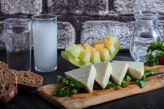 Turkish Raki with water on table with sliced melon and appetizer, traditional Turkish alcohol known as Raki, chill with friends at restaurant, dinner idea, eating and drinking concept, sitting view. High quality photo