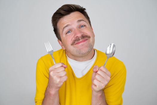 handsome hungry young man holding fork and spoon waiting for dinner. Positive facial human emotion