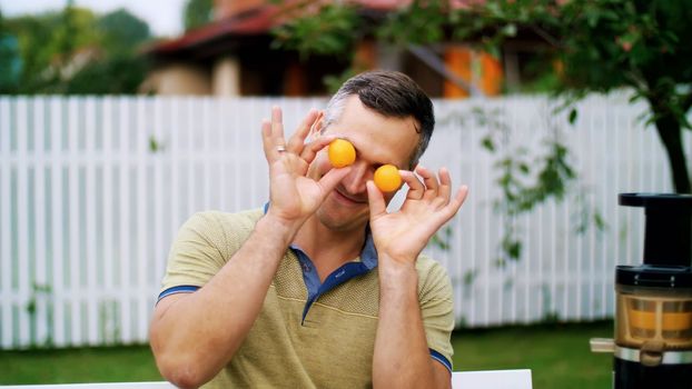 summer, in the garden. a man, father, having fun with his family outdoors, twisting, applying mandarins to his eyes. family holidays, lunch on the nature, in the courtyard. High quality photo