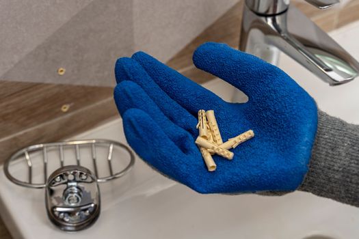 A worker's hand in protective gloves holds several plastic dowel pins in the palms against the background of the bathroom interior. renovation in the bathroom. installation of bathroom accessories.