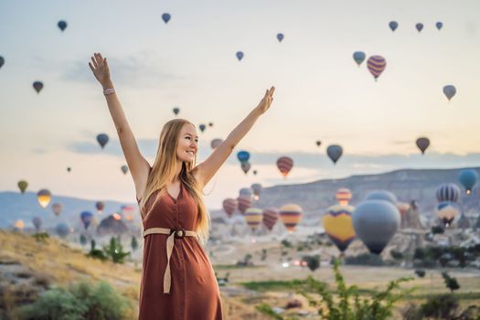 Tourist woman looking at hot air balloons in Cappadocia, Turkey. Happy Travel in Turkey concept. Woman on a mountain top enjoying wonderful view.