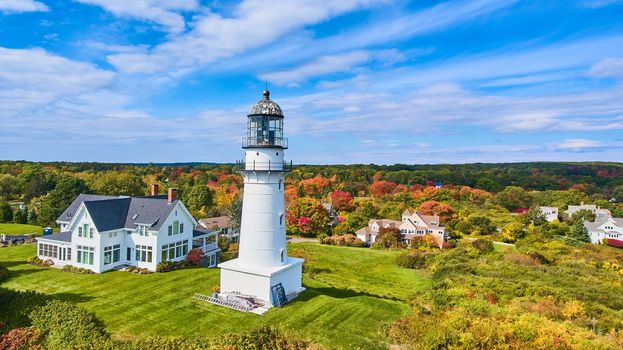 Image of Single classic white lighthouse by homes with fall foliage around