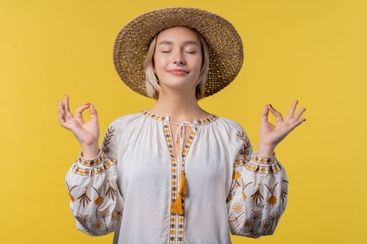 Calm ukrainian woman relaxing, meditating, refuses stress. Sunny girl breathes deeply, calms down yellow studio background. Yoga, moral balance, zen concept. High quality