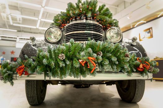 The vintage classic car is decorated with fir branches and Christmas decorations. A beautifully and stylishly decorated car shines with an outfit for Christmas and New Year.