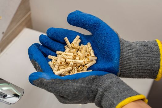 The hands of a worker in protective gloves hold a bunch of plastic dowel pins in their palms against the background of the bathroom interior. renovation in the bathroom. installation of bathroom accessories.
